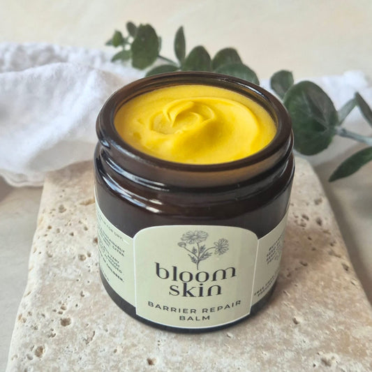 Jar of 'bloom skin' barrier repair balm with yellow cream on a stone surface.