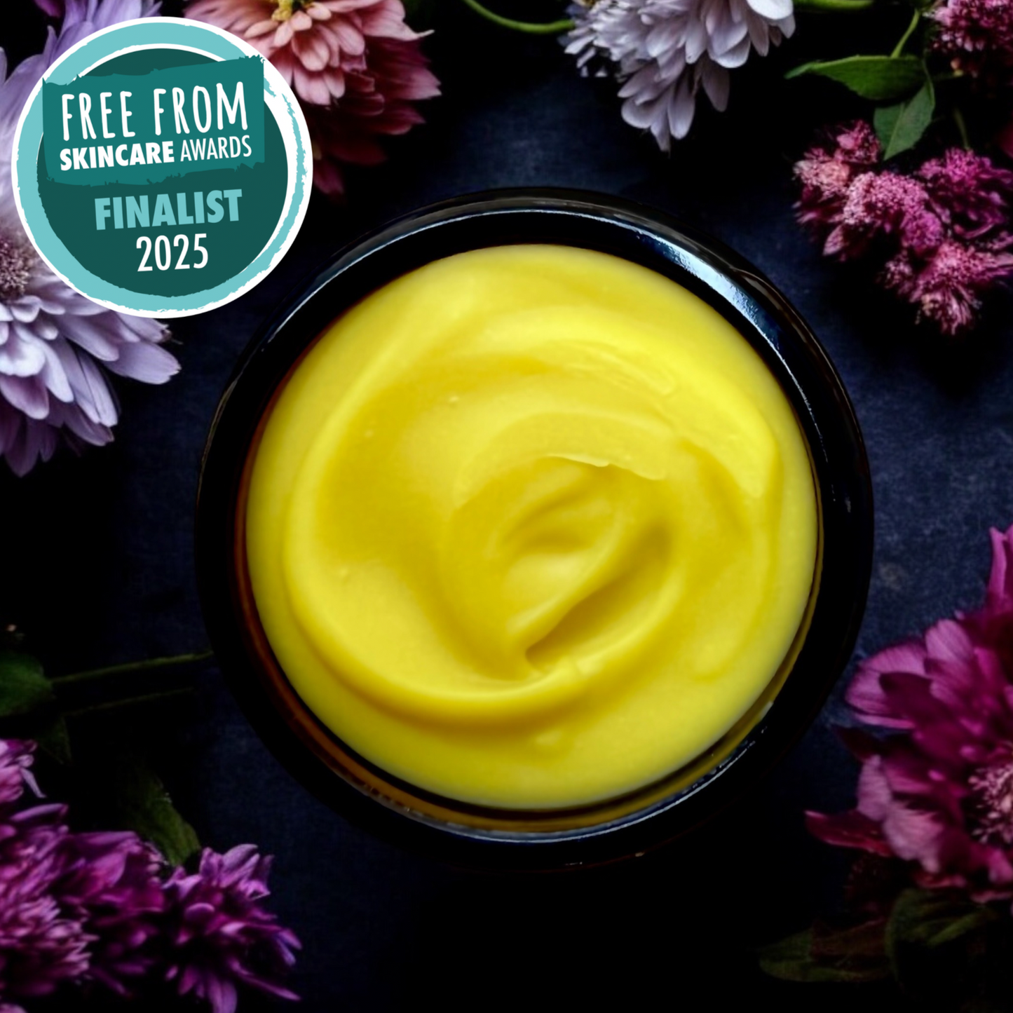 Yellow cream in a black container surrounded by purple flowers.