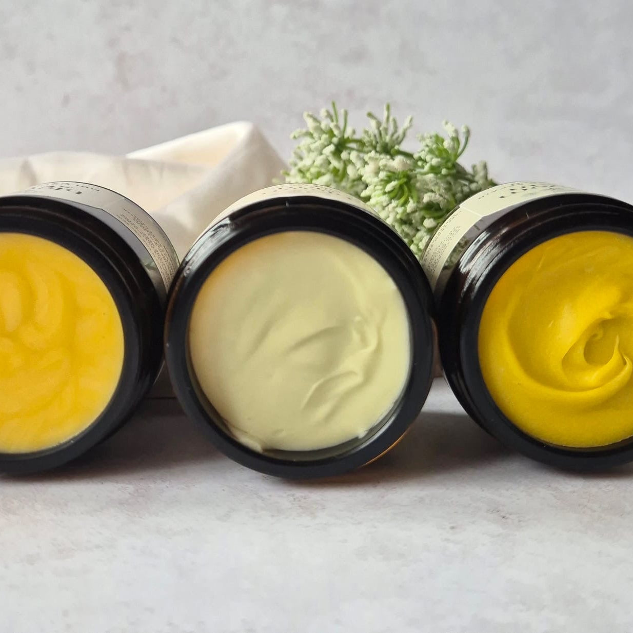 Three jars of yellow cream on a light surface with a neutral background