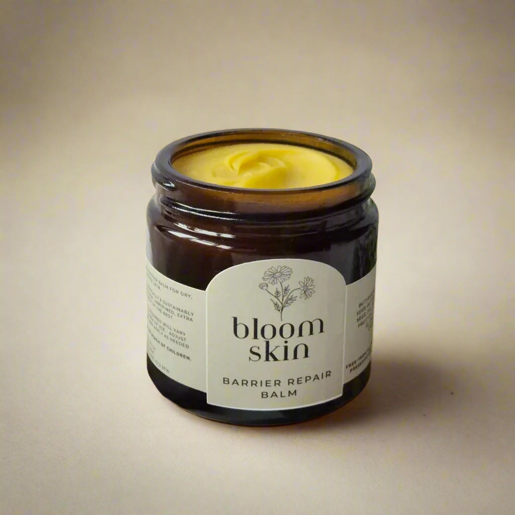 Jar of 'bloom skin' barrier repair balm on a wooden board with flowers in the background