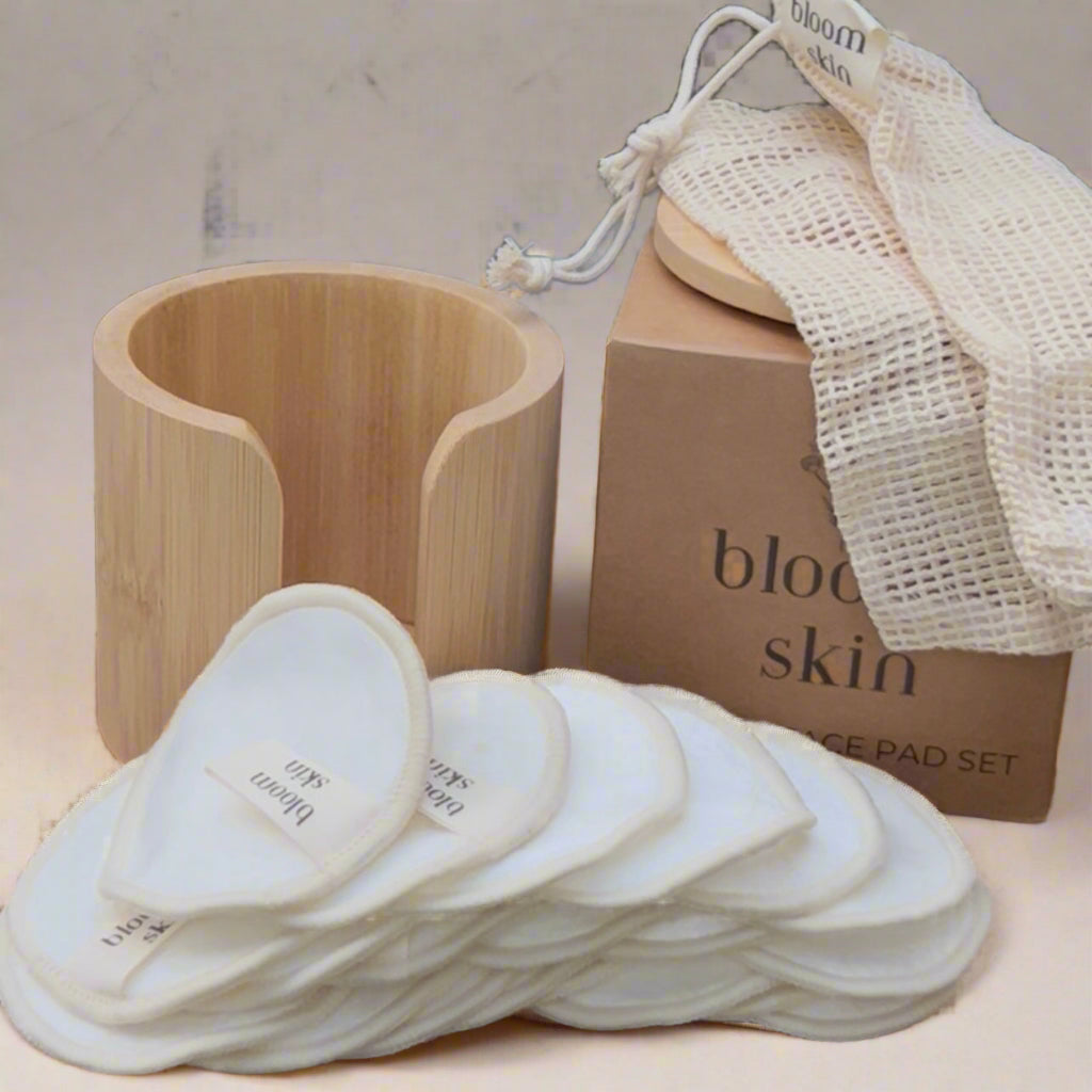 Bamboo products including a wooden holder, cotton pads, and a branded box on a woven surface with plants in the background.