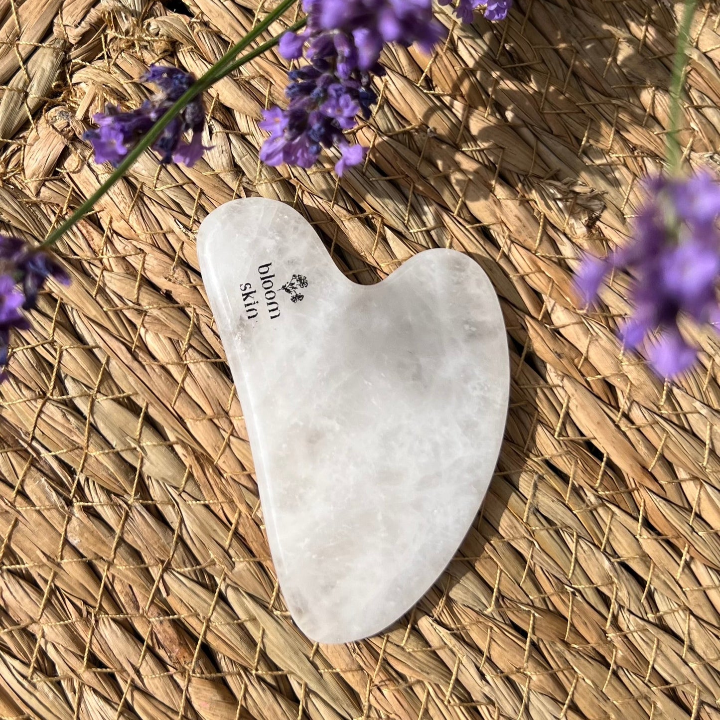 White gua sha tool on a woven surface with lavender flowers