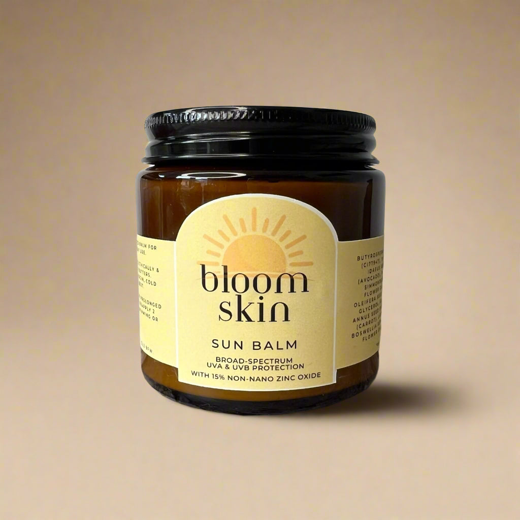 A jar of Bloom Skin Sun Balm with a label showing the brand name and 'Sun Balm' product title, placed on a wooden surface outdoors.