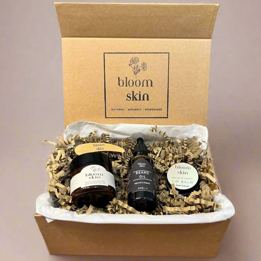Gift set from 'bloom skin' with bottles and a box on a wooden surface with plants in the background.