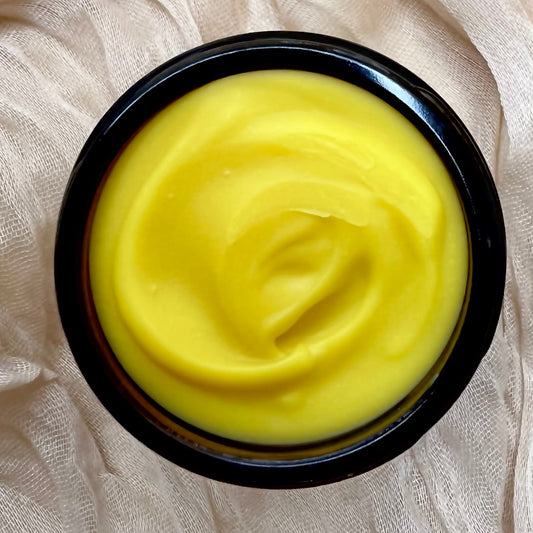Yellow cream in a black container on a textured white fabric background
