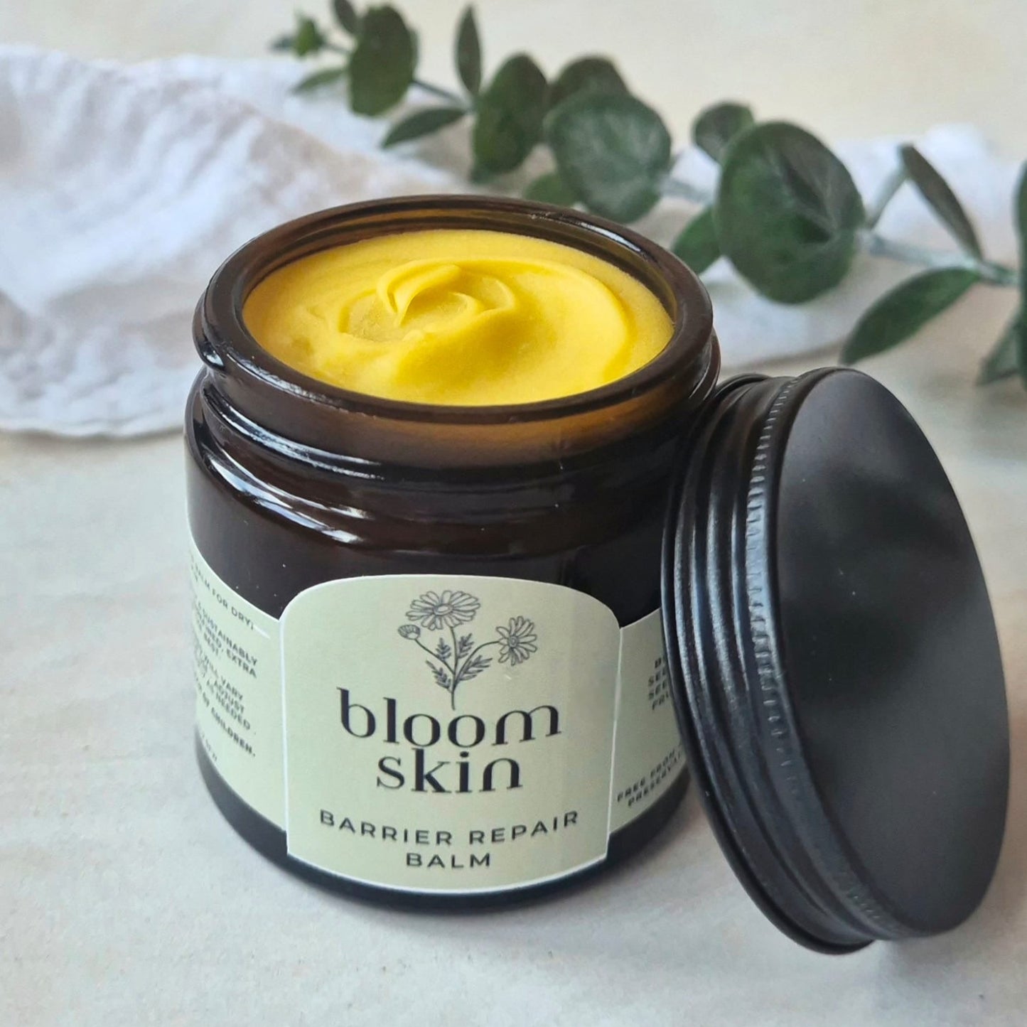 Jar of 'bloom skin' barrier repair balm with a black lid on a light background