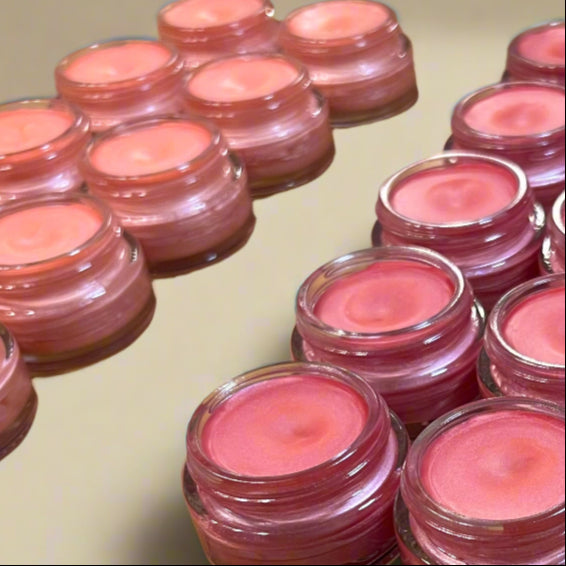 Multiple small jars of pink lip balm arranged on a wooden surface