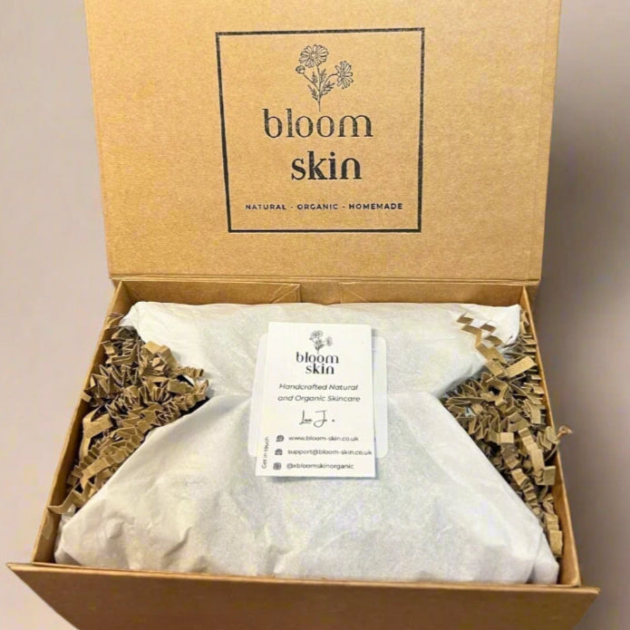 Bloom Skin product packaging on a wooden surface with plants in the background
