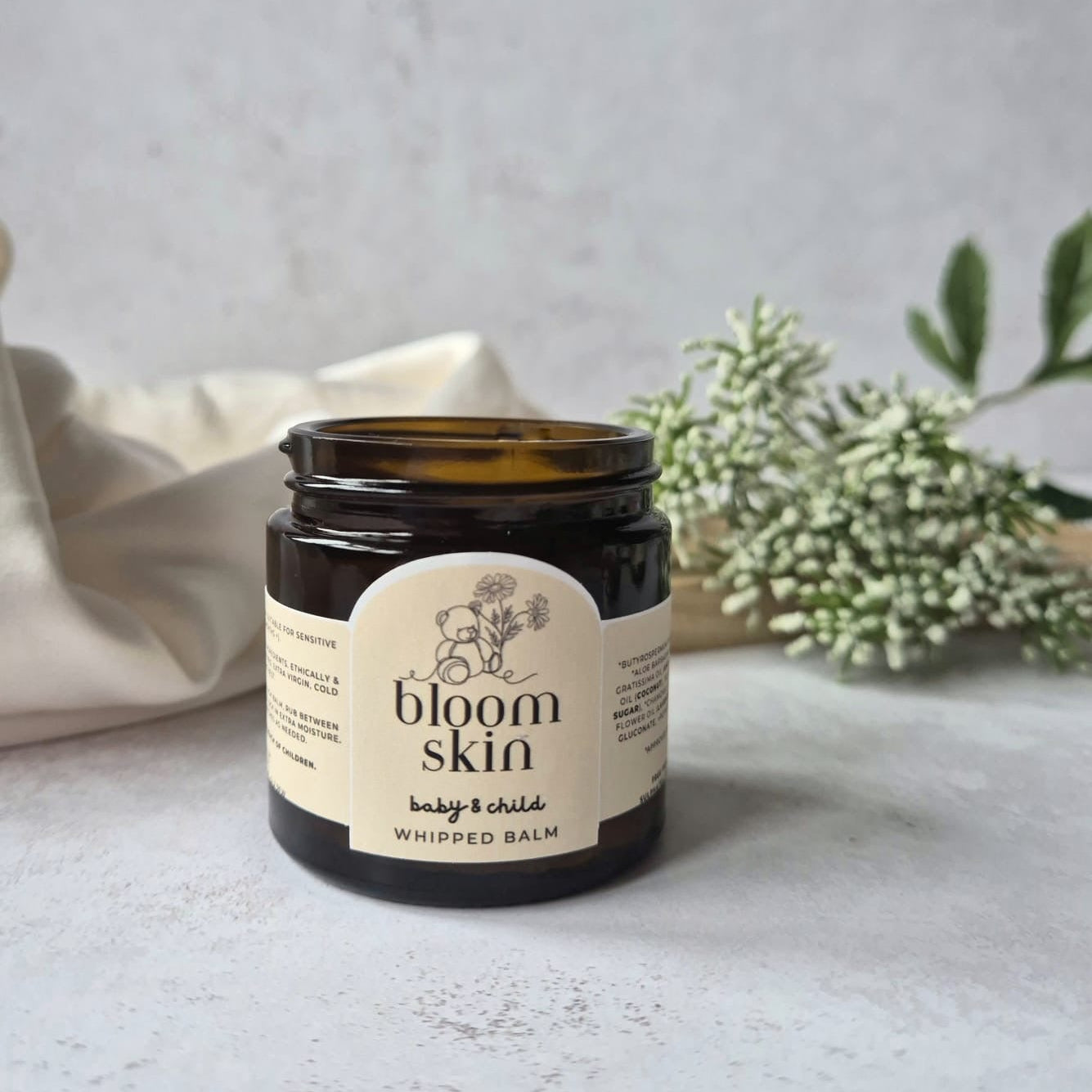 Jar of 'bloom skin' whipped balm on a light surface with a neutral background