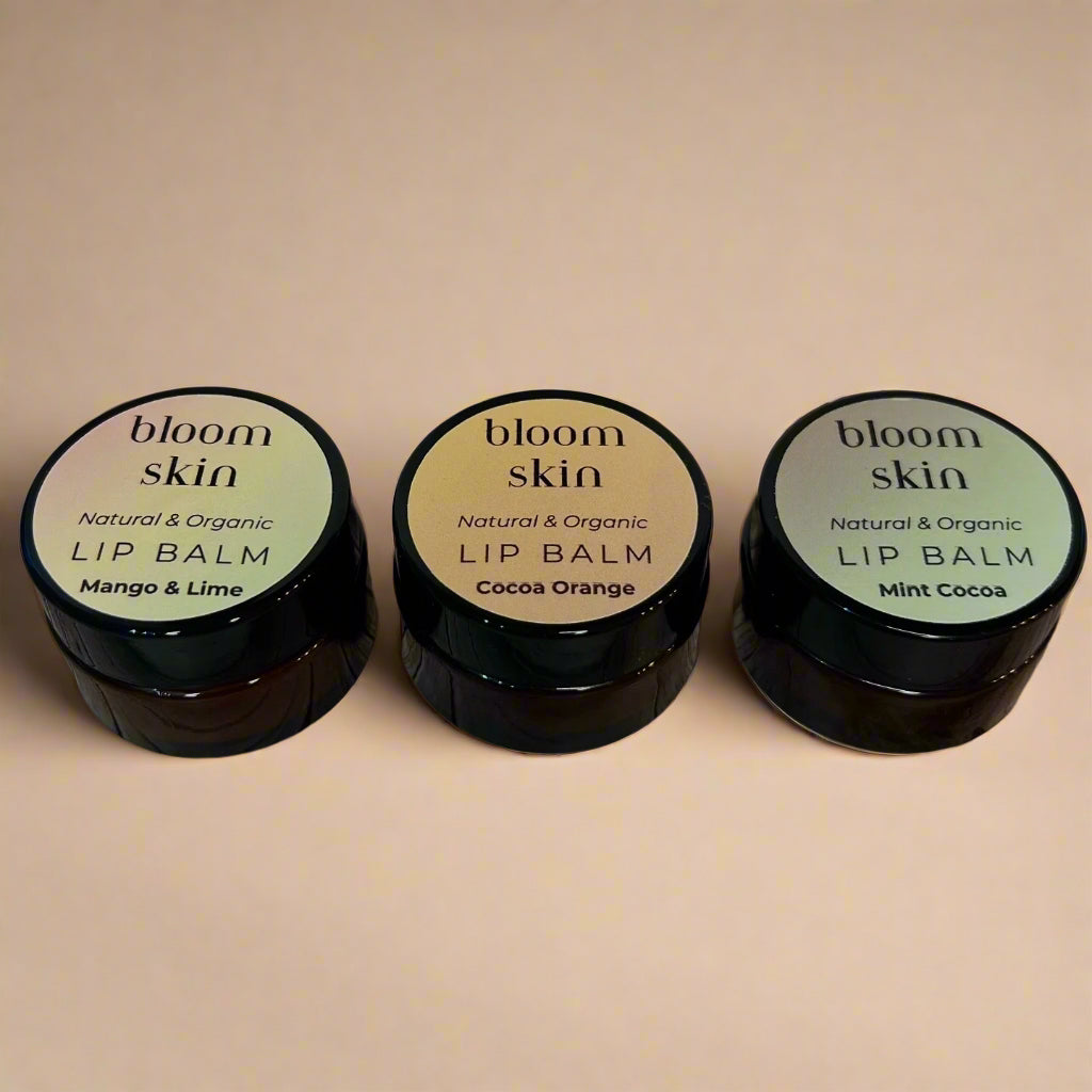 Three lip balm containers labeled 'Mango & Lime', 'Cocoa Orange', and 'Mint Cocoa' on a wooden surface.