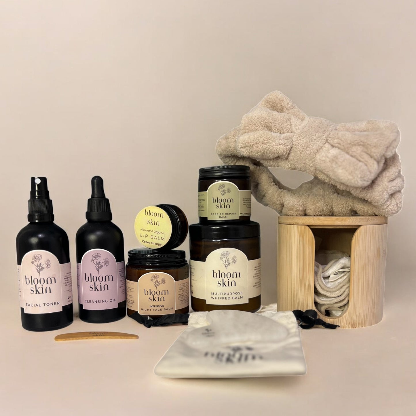Collection of 'bloom skin' skincare products including bottles, jars, and a towel on a neutral background.