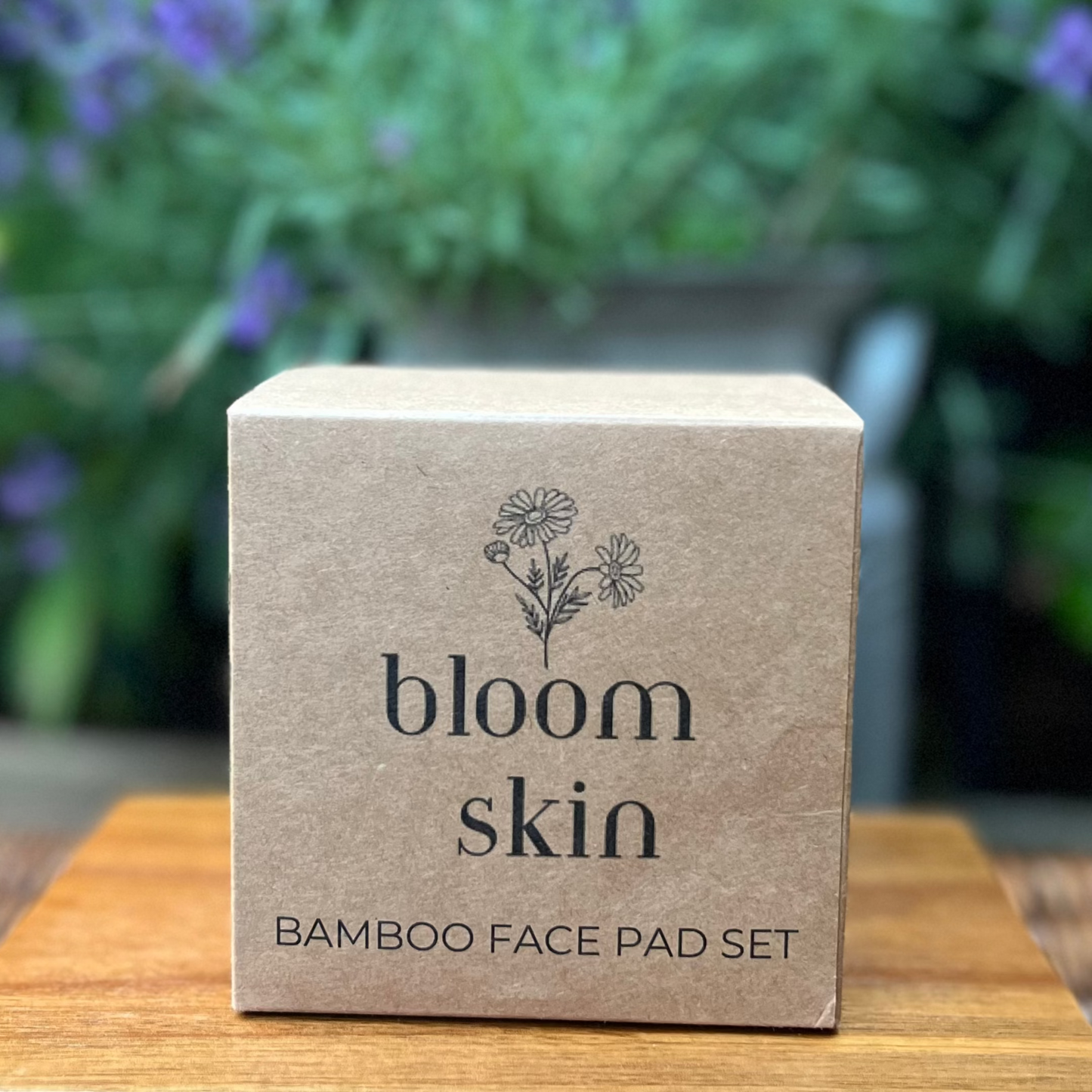 Bamboo face pad set packaging with 'bloom skin' branding on a wooden surface with a blurred floral background.