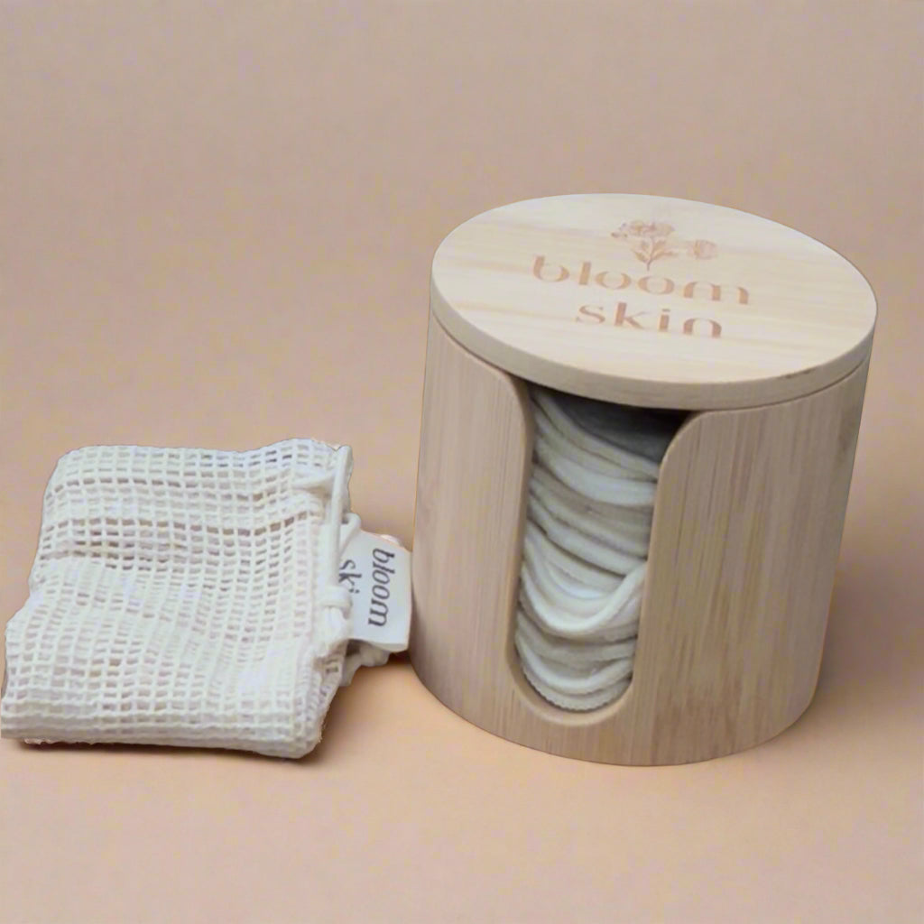 Wooden container with cotton pads, a white cloth, and lavender plant on a wooden surface.