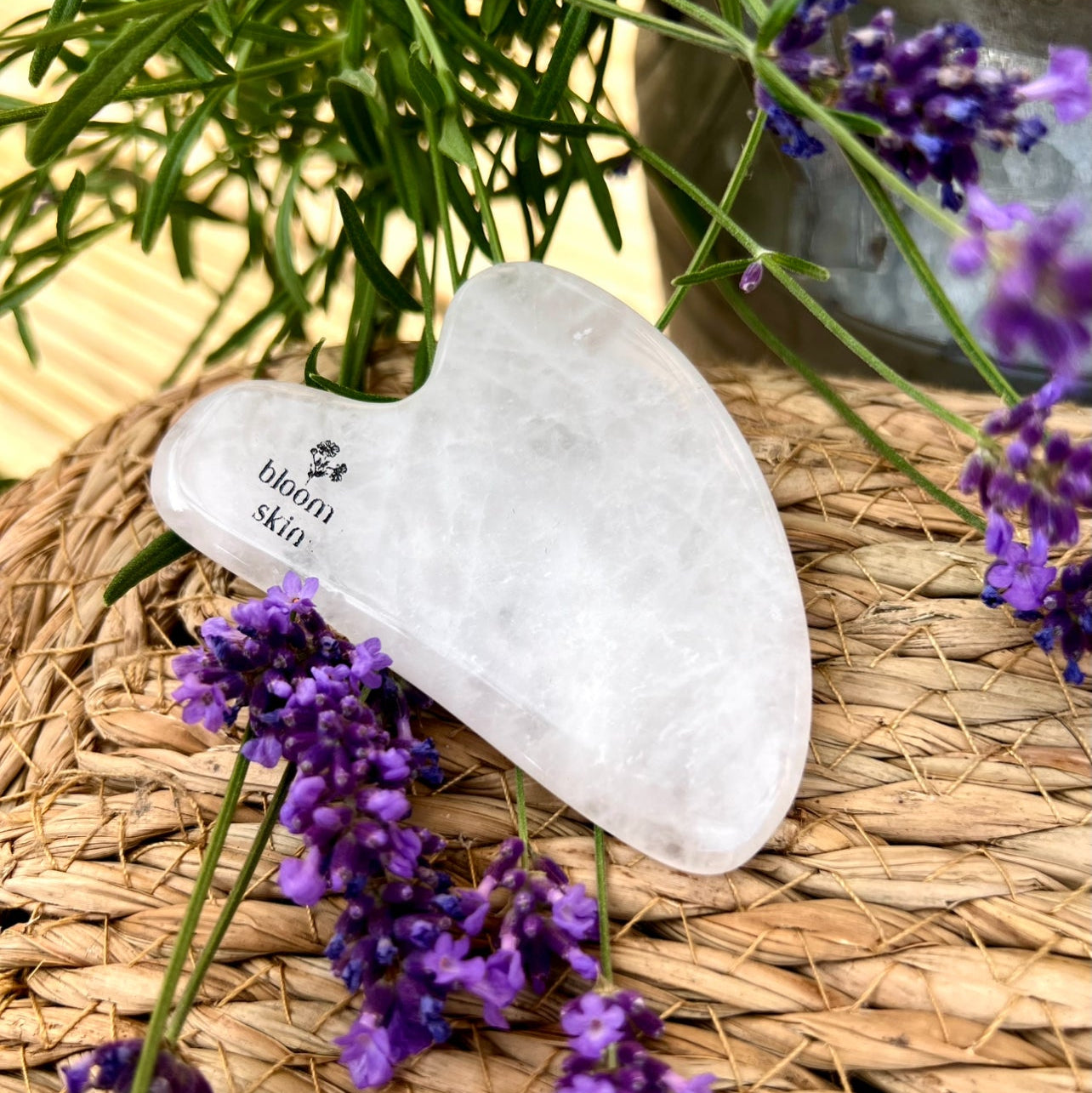Gua Sha tool with 'bloom skin' branding on a woven mat with lavender flowers.