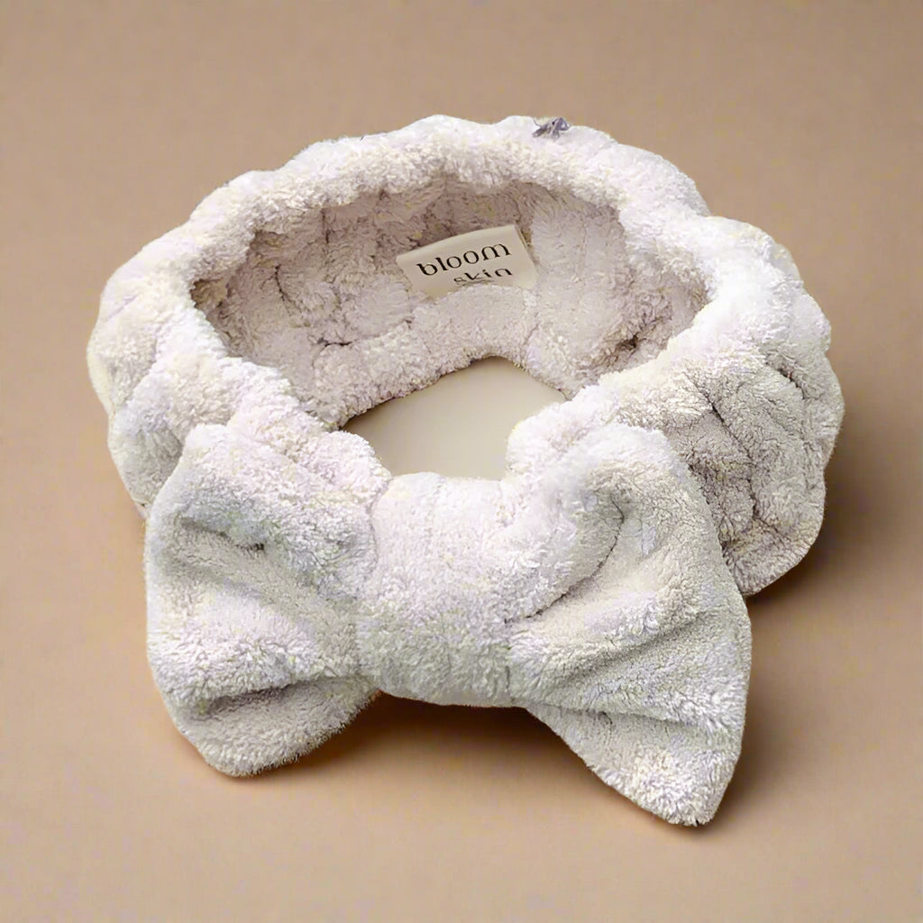 Fluffy white headband with a bow on a woven surface with lavender flowers in the background