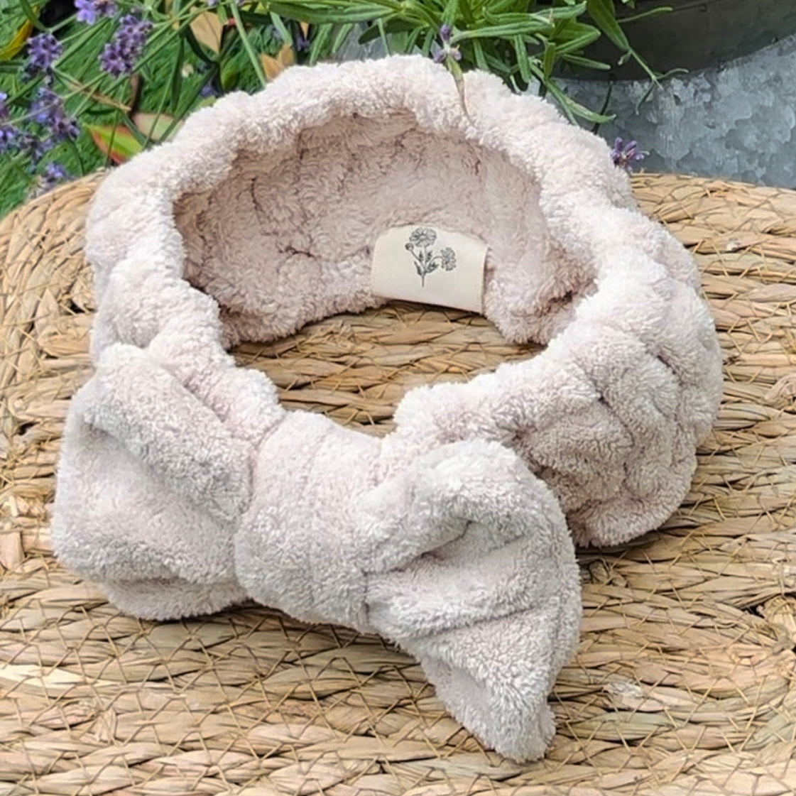 Fluffy beige headband with a bow on a woven surface with lavender in the background
