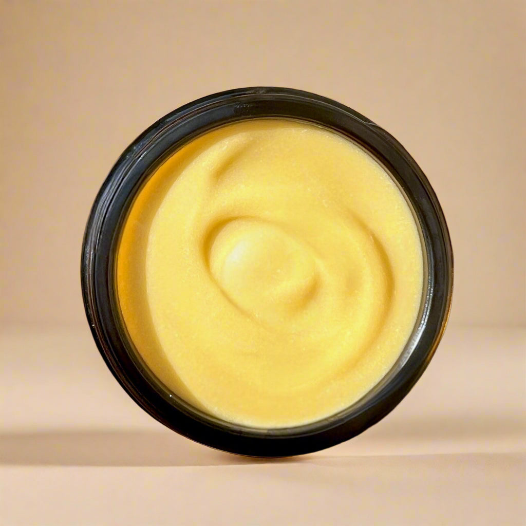 Yellow cream in a black container on a wooden board with flowers and oranges