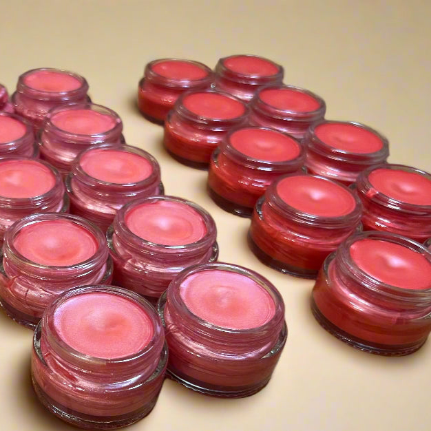Multiple small jars of pink lip balm on a wooden surface