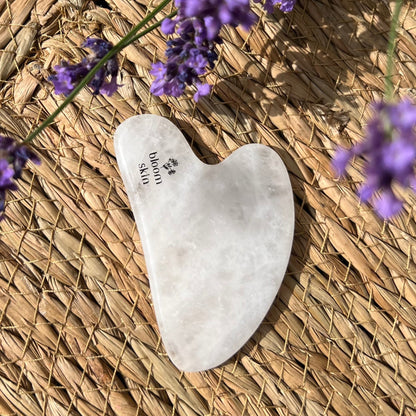 White gua sha tool on a woven surface with lavender flowers