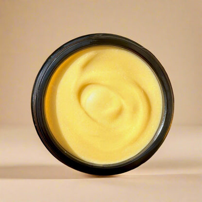 Yellow cream in a black container on a wooden board with flowers and oranges